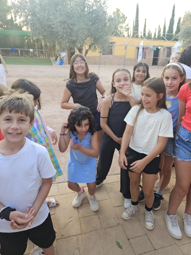 A group of smiling children posing together outdoors on a brick patio with trees in the background.