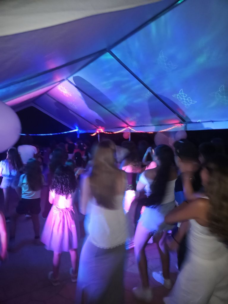 Crowded party under a lit tent with blue and purple glow as people dance.