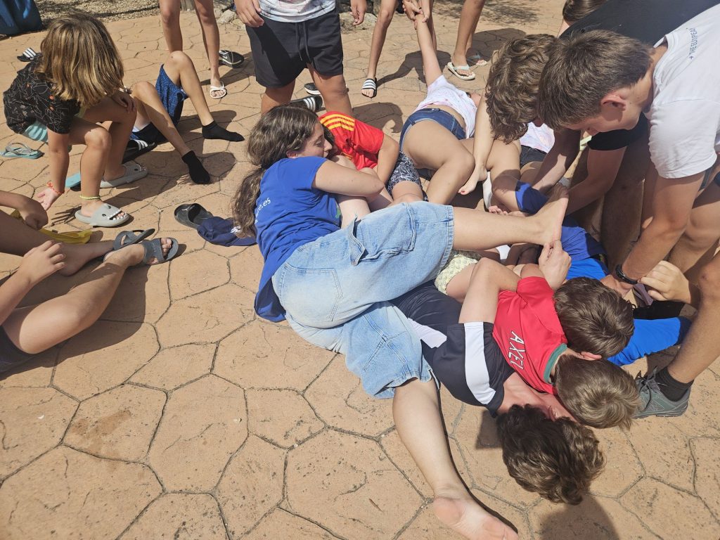 Group of children lying on a cracked patio in a circle, entwined hands, playing a group game outdoors