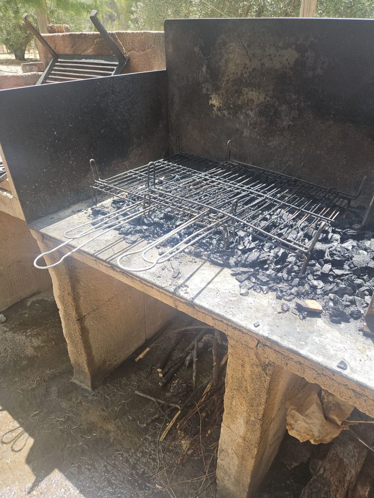 Outdoor charcoal barbecue grill with a metal grate over hot, ashy coals inside a stone brick pit.